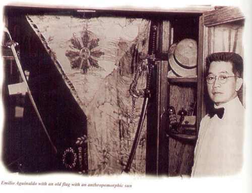 Si Heneral Aguinaldo sa harap ng pinaniniwalaang unang watawat ng Pilipinas.  Mula sa Tahanan ng Kasarinlan.