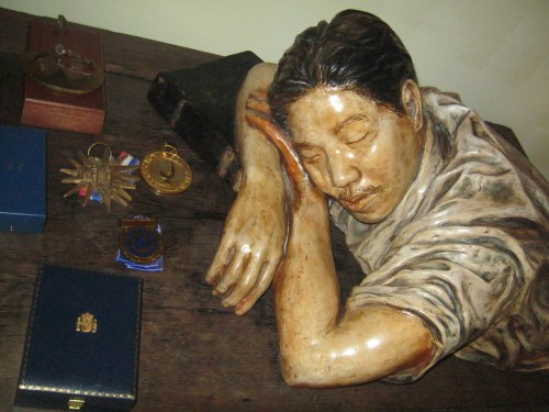 Si Ambeth Ocampo na natutulog.  Obra ni julie Lluch-Dalena.  Ang obra ay nasa tabi ng ilan sa mga dekorasyon at parangal na iginawad kay Sir Ambeth, kumbaga, "resting on his laurels."