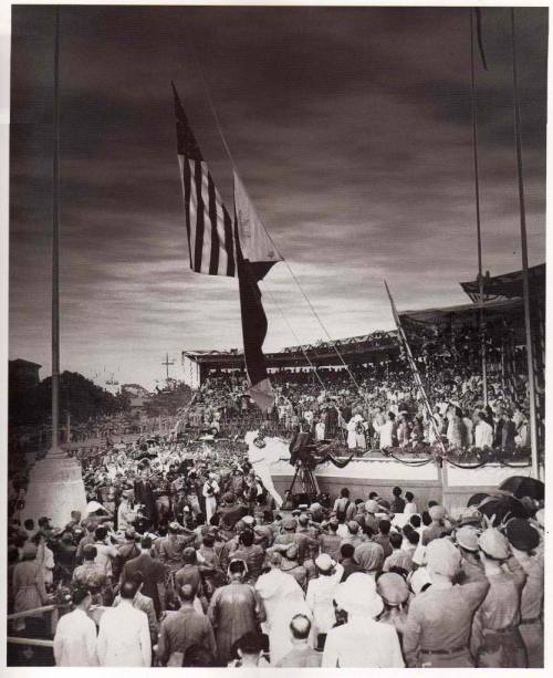 Ang pagbaba ng bandila ng Amerika at ang pagtataas ng watawat ng Pilipinas sa flagpole sa harapan ng Monumento ni Rizal (natatakpan ng entablado) noong July 4, 1946.  Mula sa gov.ph.