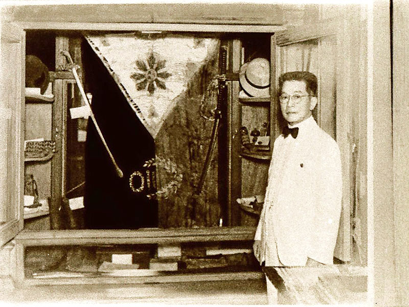 Si Heneral Emilio Aguinaldo sa harapan ng Aguinaldo-Suntay flag na siyang pinaniniwalaan ng ilan na isa sa pinakaunang, kung hindi man ang pinakaunang watawat ng Pilipinas.