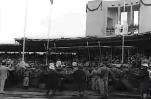 Ang pansamantalang grandstand na tinakpan ang Rizal Monument sa harapan  ng flagpole sa Luneta.  Mula sa newsreel na "Philippine Independence."