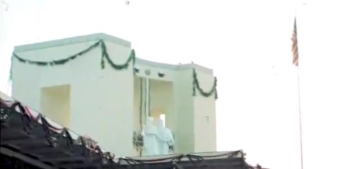 Ang pansamantalang grandstand na tinakpan ang Rizal Monument sa harapan  ng flagpole sa Luneta.  Mula sa newsreel ng FitchettFilm.com.